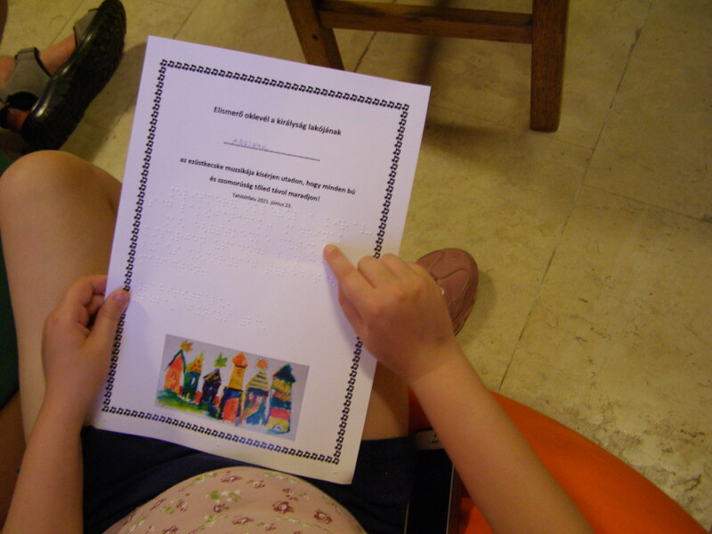 MOL pályázat, nyári táborban vak gyermek Braille írást olvas az oklevélen